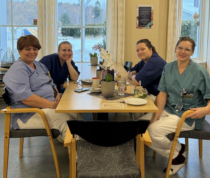 4 damer i sykehjemsuniformer sitter rundt et bord og spiser lunsj