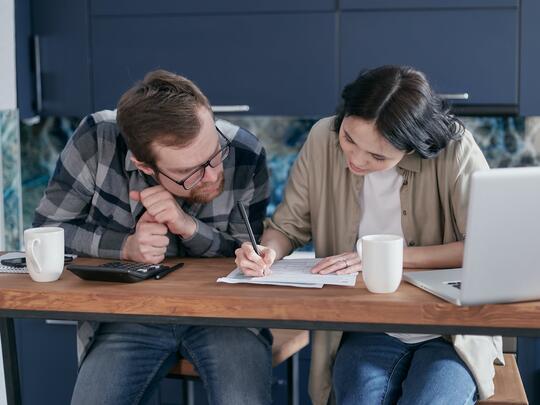 En kvinne og en mann sitter bøyd over et bord og skriver på ark