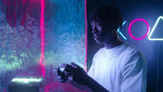 En ung mann holder en spillkonsoll og gamer i ett mørkt rom med neonlys bak seg